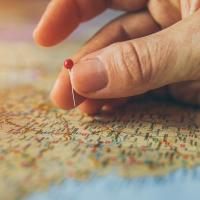Hand pinpointing a location on a map with a pin